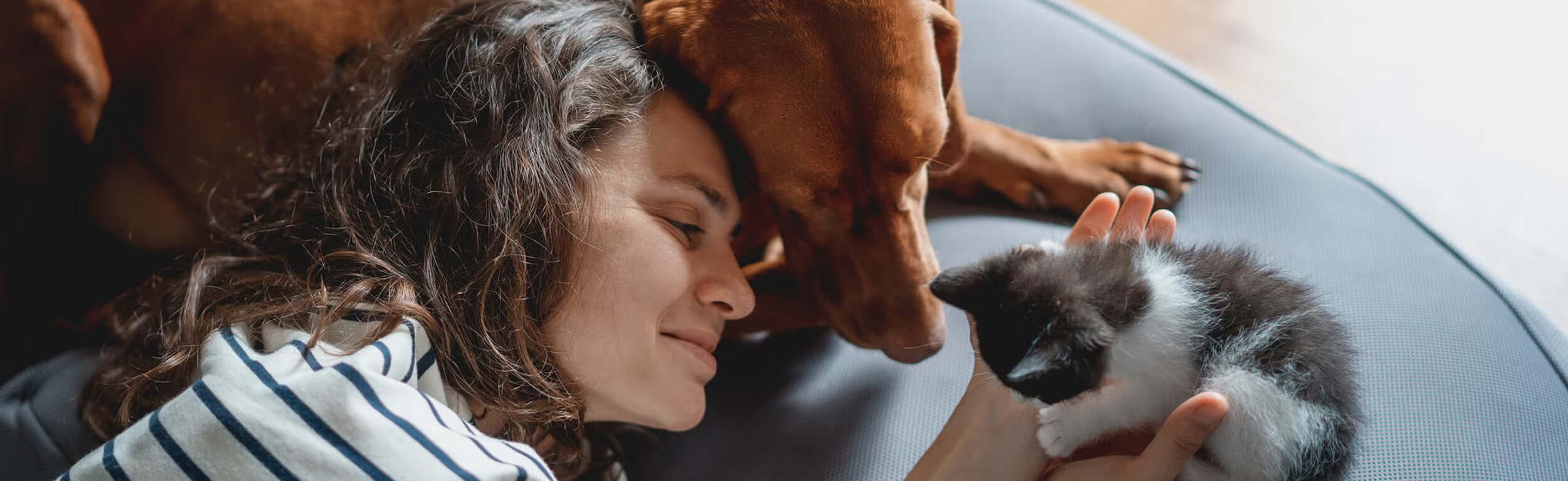 lady cuddling her cat and dog smiling contently.