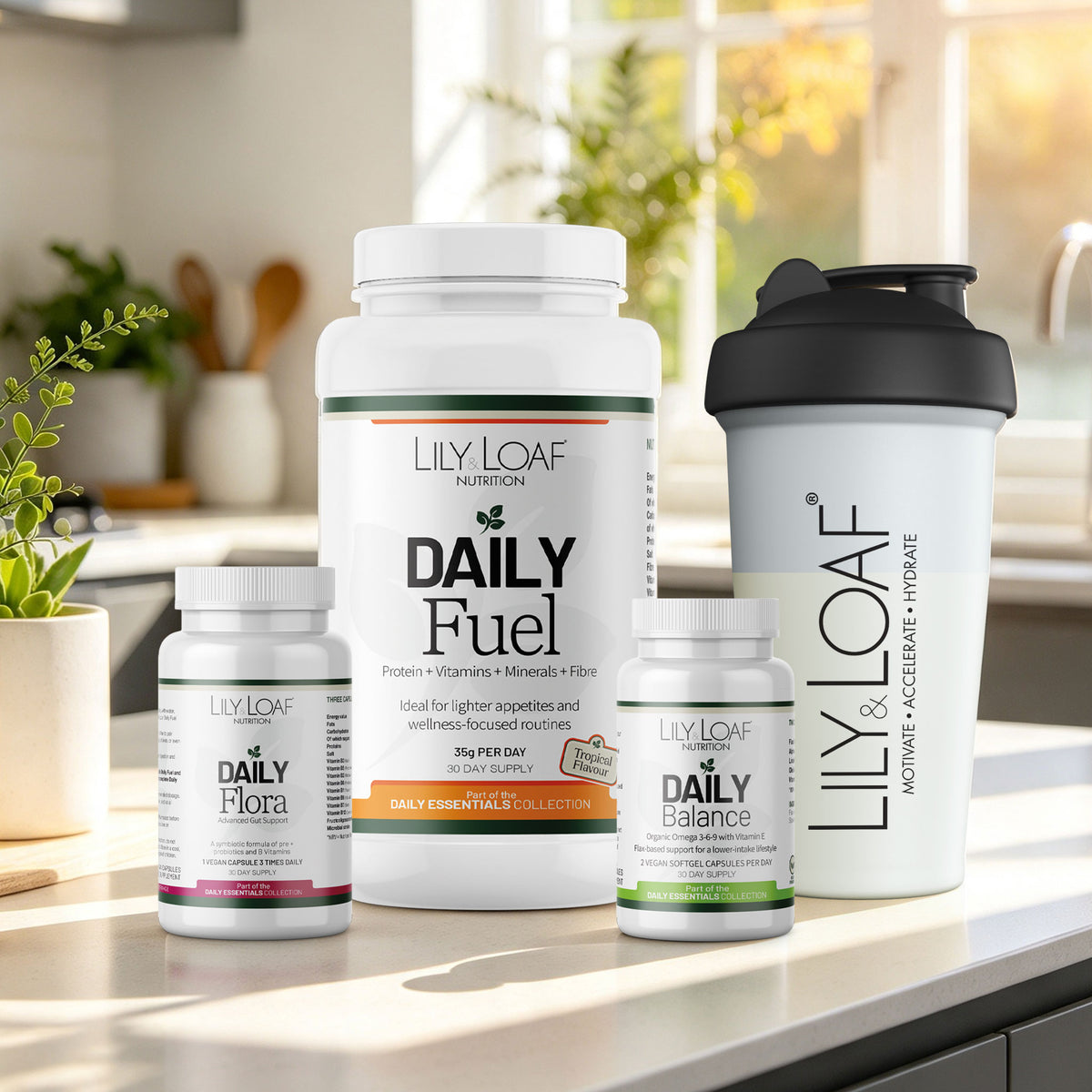 Lily & Loaf Daily Essentials products arranged on a kitchen counter, including a large Daily Fuel supplement bottle, a Daily Flora bottle, a Daily Balance bottle, and a white shaker bottle with a black lid. 