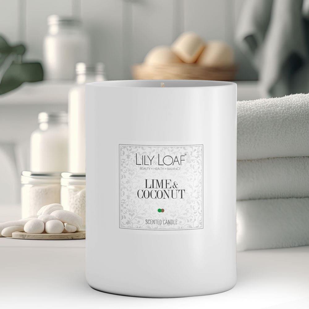Lily & Loaf Lime & Coconut Soy Wax Candle on a bathroom counter with a stack of fluffy white towels and lotions in pots in the background