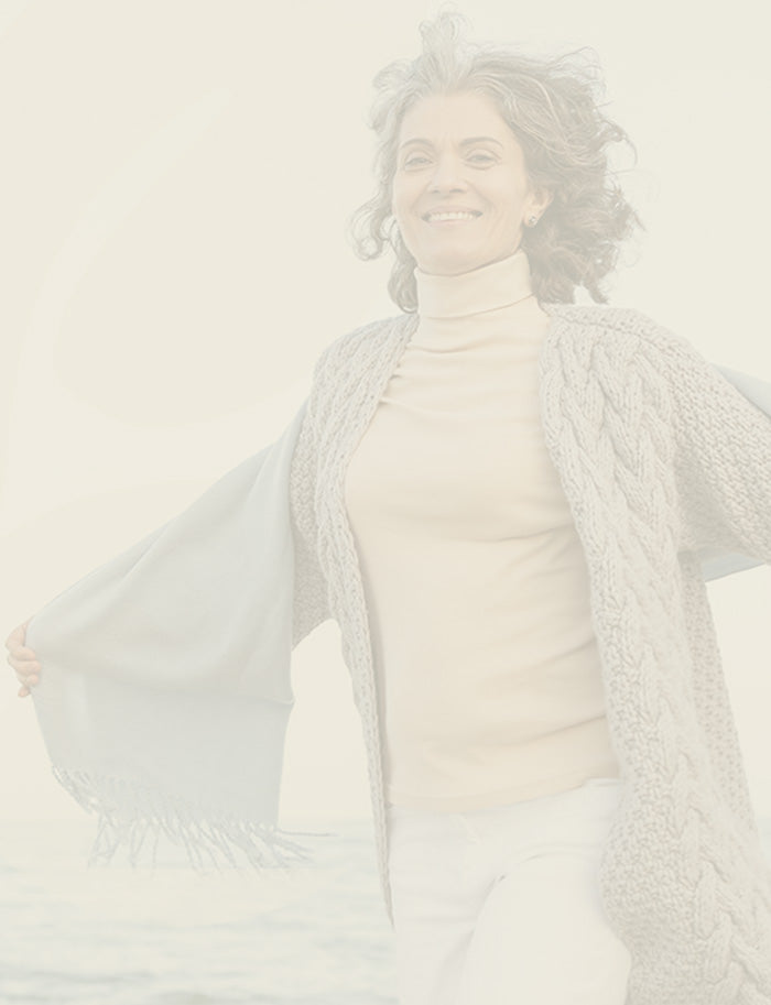 Woman wearing a light gray cardigan over a beige top on a plain background