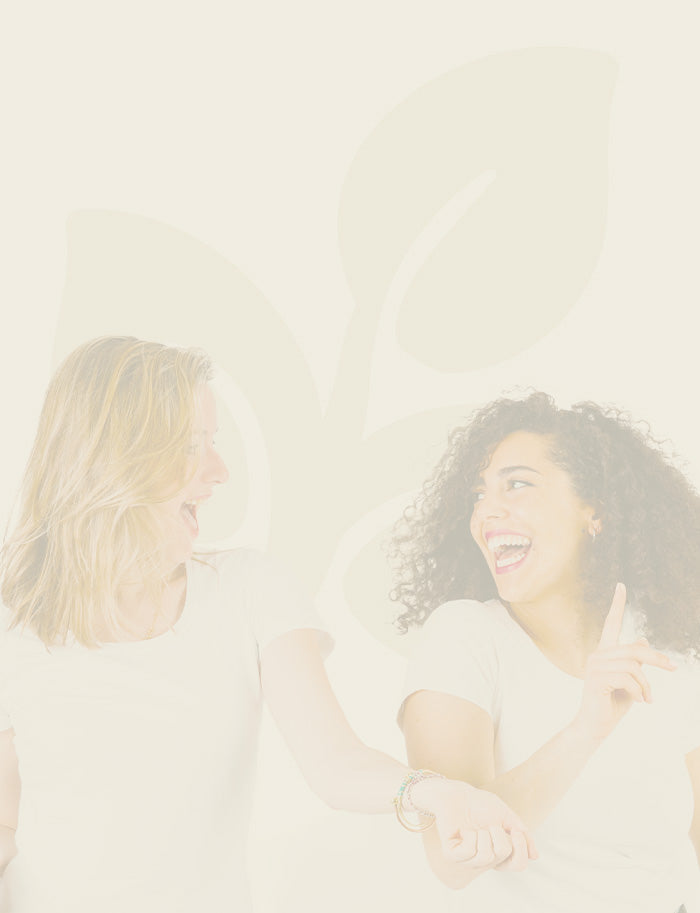 Two women sitting close together, smiling and holding hands against a light background