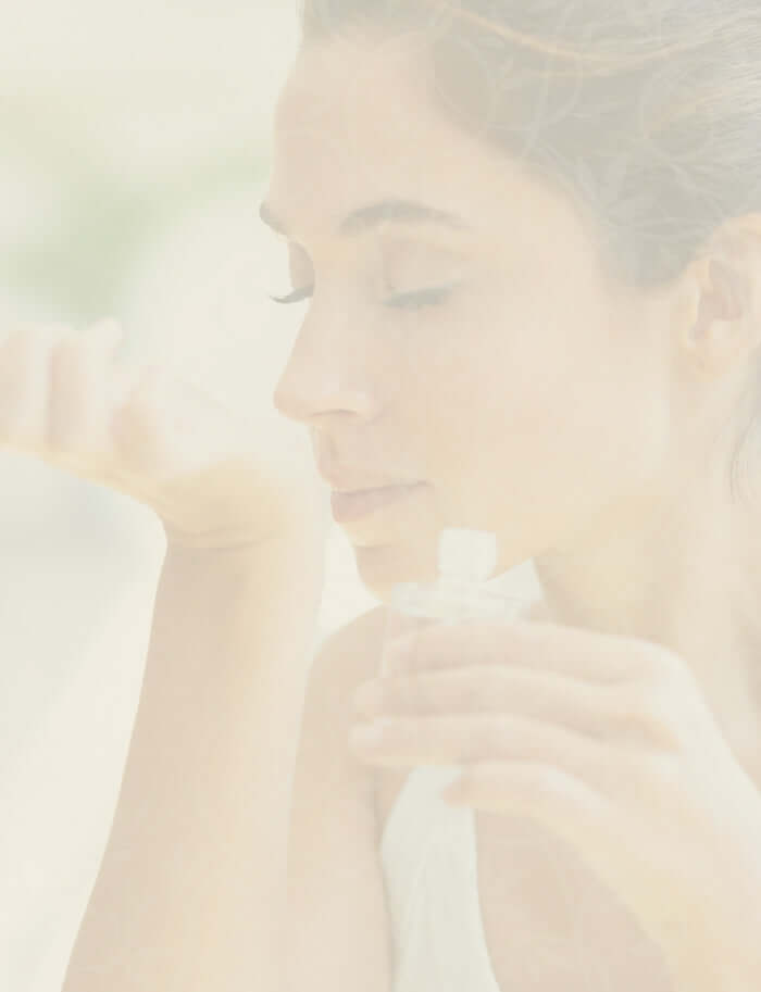 Woman holding her wrist to her nose smelling fragrance with a soft, blurred background
