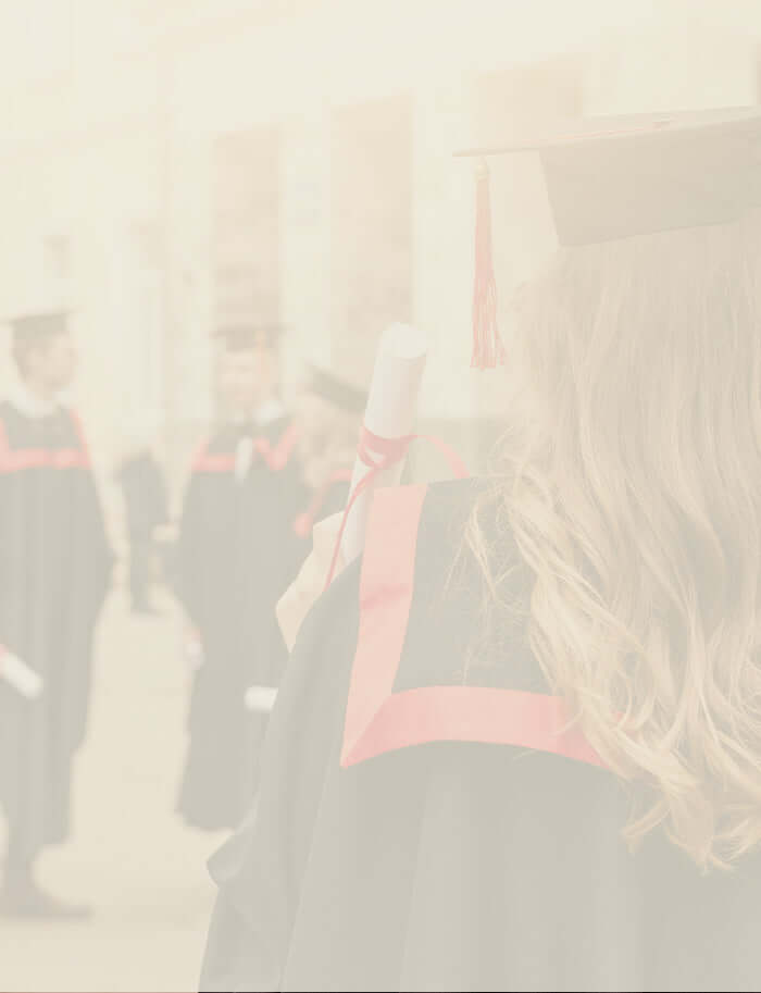 A graduate in cap and gown holding a diploma, with other graduates blurred in the background.