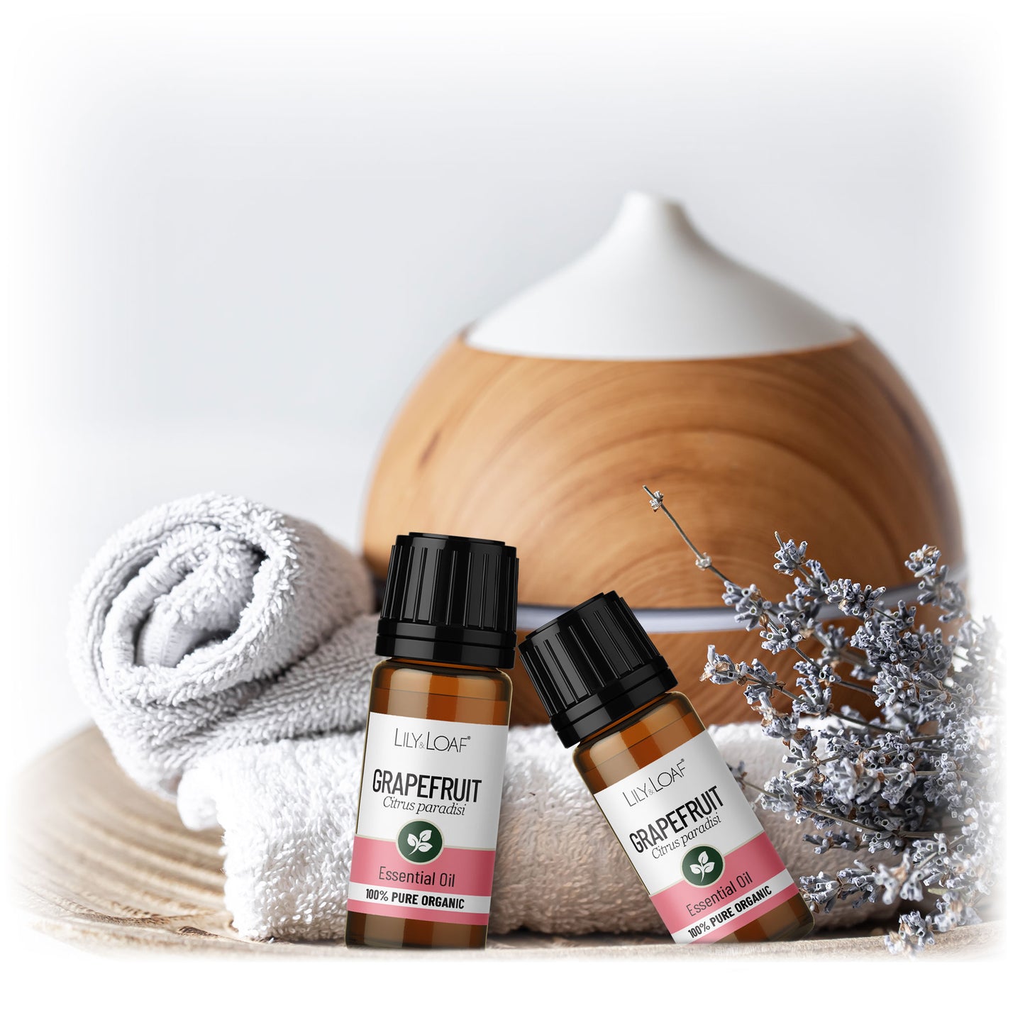 Lily & Loaf Grapefruit essential oil bottles beside diffuser, rolled towel and dried florals, calming aromatherapy scene.