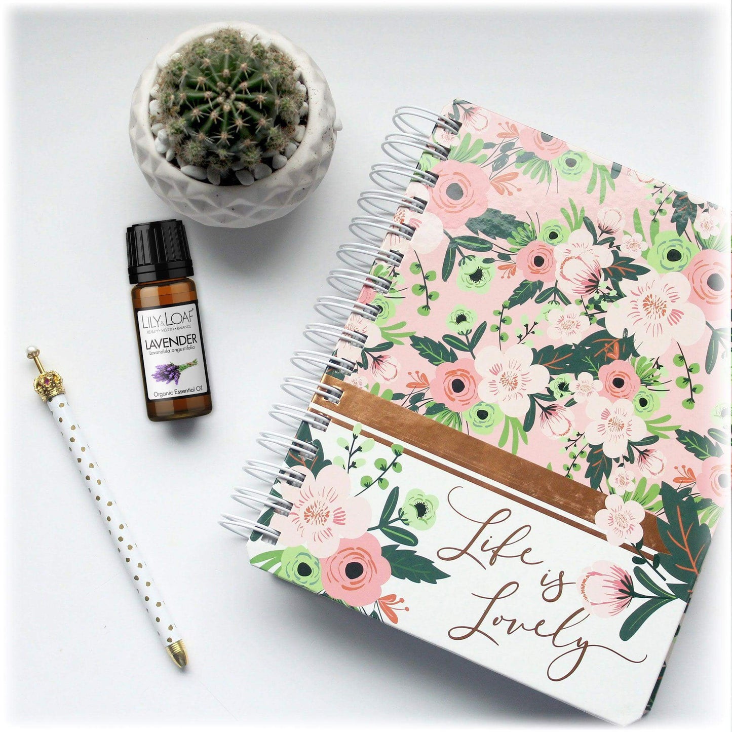 Lavender Essential Oil next to a floral diary, pen and cactusies.