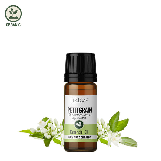 Lily & Loaf Organic Petitgrain Essential Oil in amber glass bottle with green leaves and white flowers on a white background.