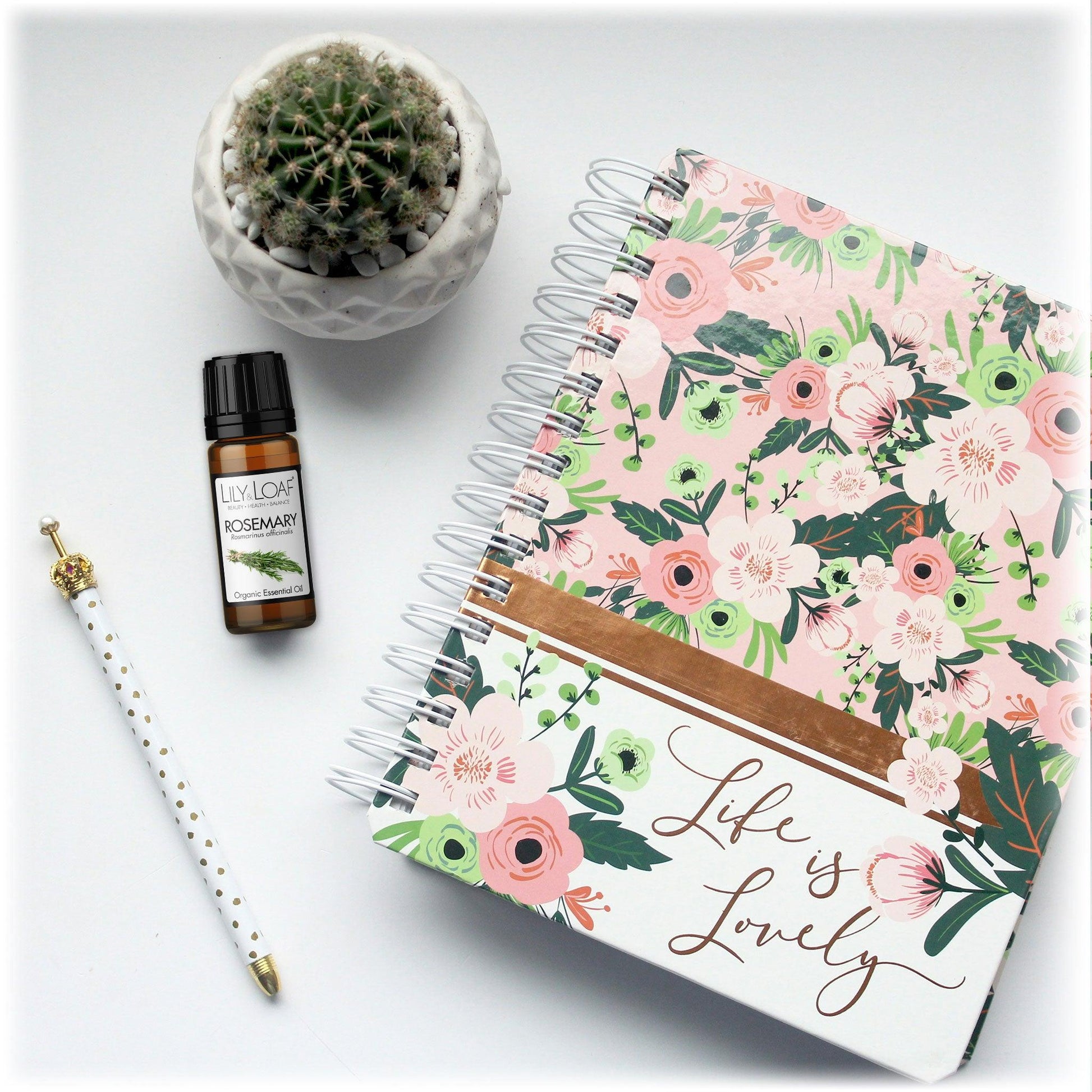 Lily & Loaf Rosemary Organic Essential Oil bottle next to a floral notebook, pen, and potted cactus. Enhances focus and mental clarity for productivity.