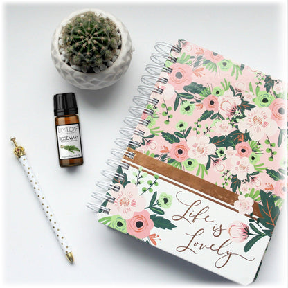 Lily & Loaf Rosemary Organic Essential Oil bottle next to a floral notebook, pen, and potted cactus. Enhances focus and mental clarity for productivity.