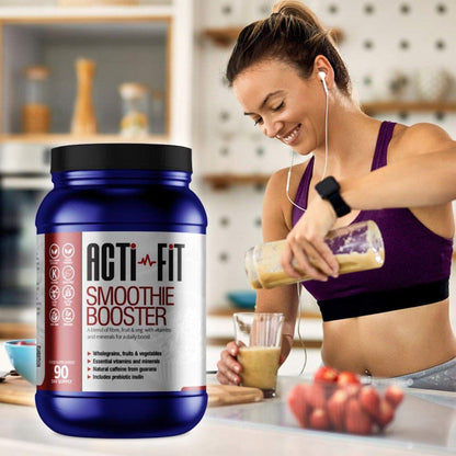Woman in sportswear pouring a smoothie in a kitchen, with Acti-Fit Smoothie Booster tub displayed beside fresh fruit.