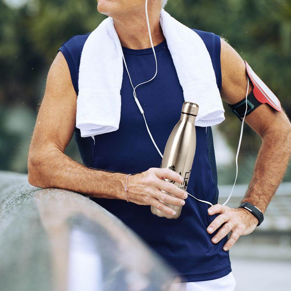 Active man outdoors wearing earphones and armband, holding a Lily & Loaf stainless steel water bottle during exercise.