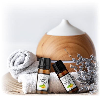 Lily & Loaf Ylang Ylang III essential oil bottles with a diffuser, rolled towel, and lavender sprig, promoting a calming and relaxing spa atmosphere.